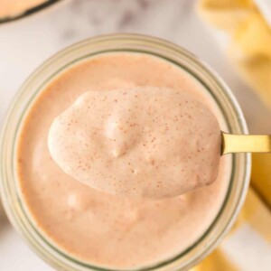small glass jar of Alabama white sauce being spooned out with a golden spoon.