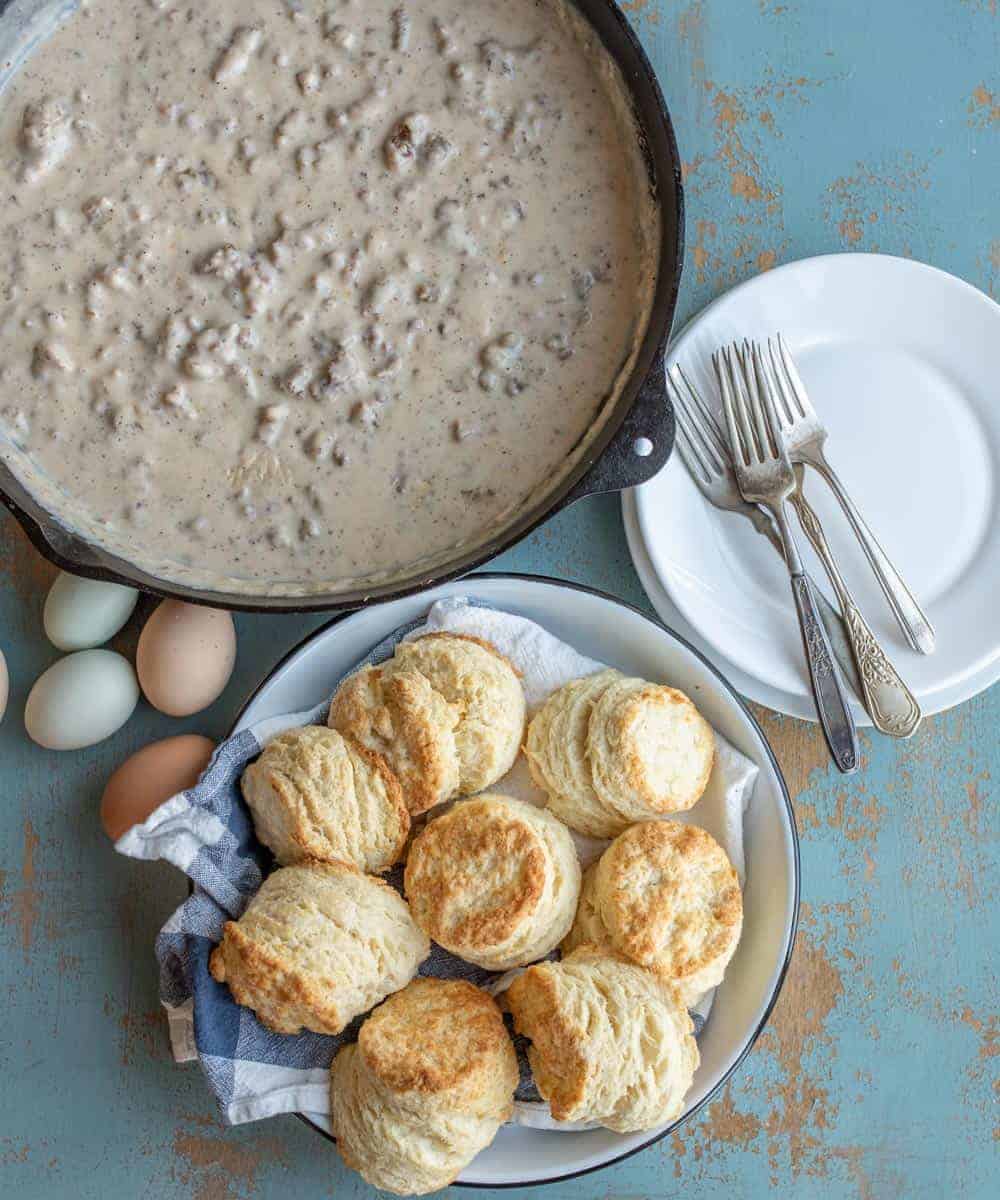 cast iron skillet with sausage gravy and a white plate with a biscuit and gravy.