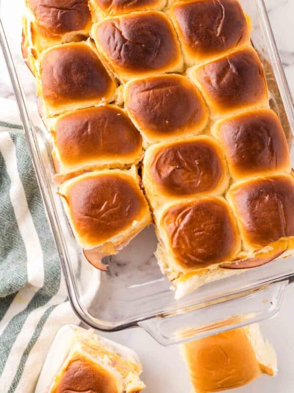 casserole dish with baked ham and cheese sliders on hawaiian rolls.