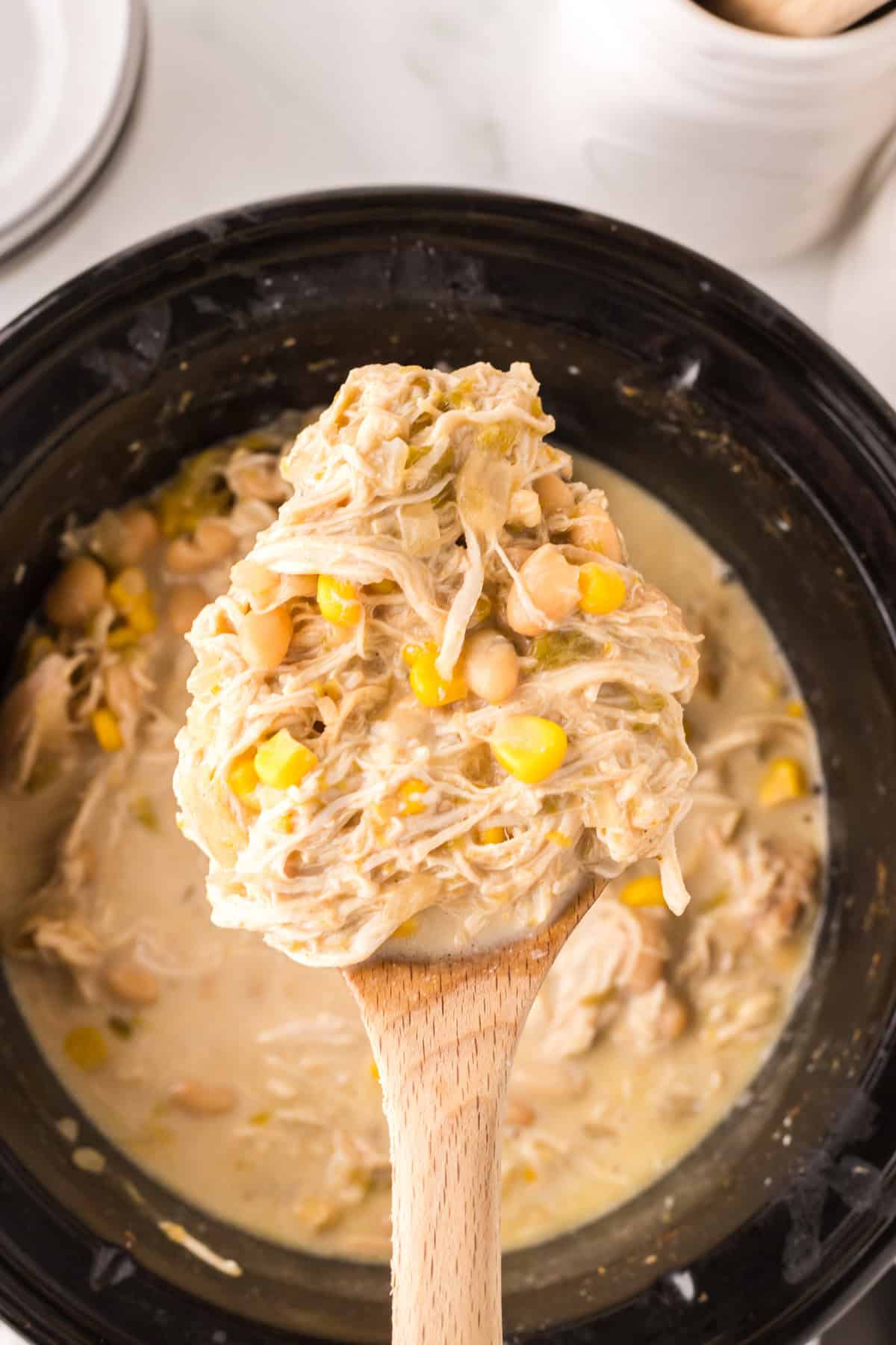 crock pot with white chicken chili recipe inside on a wooden spoon.